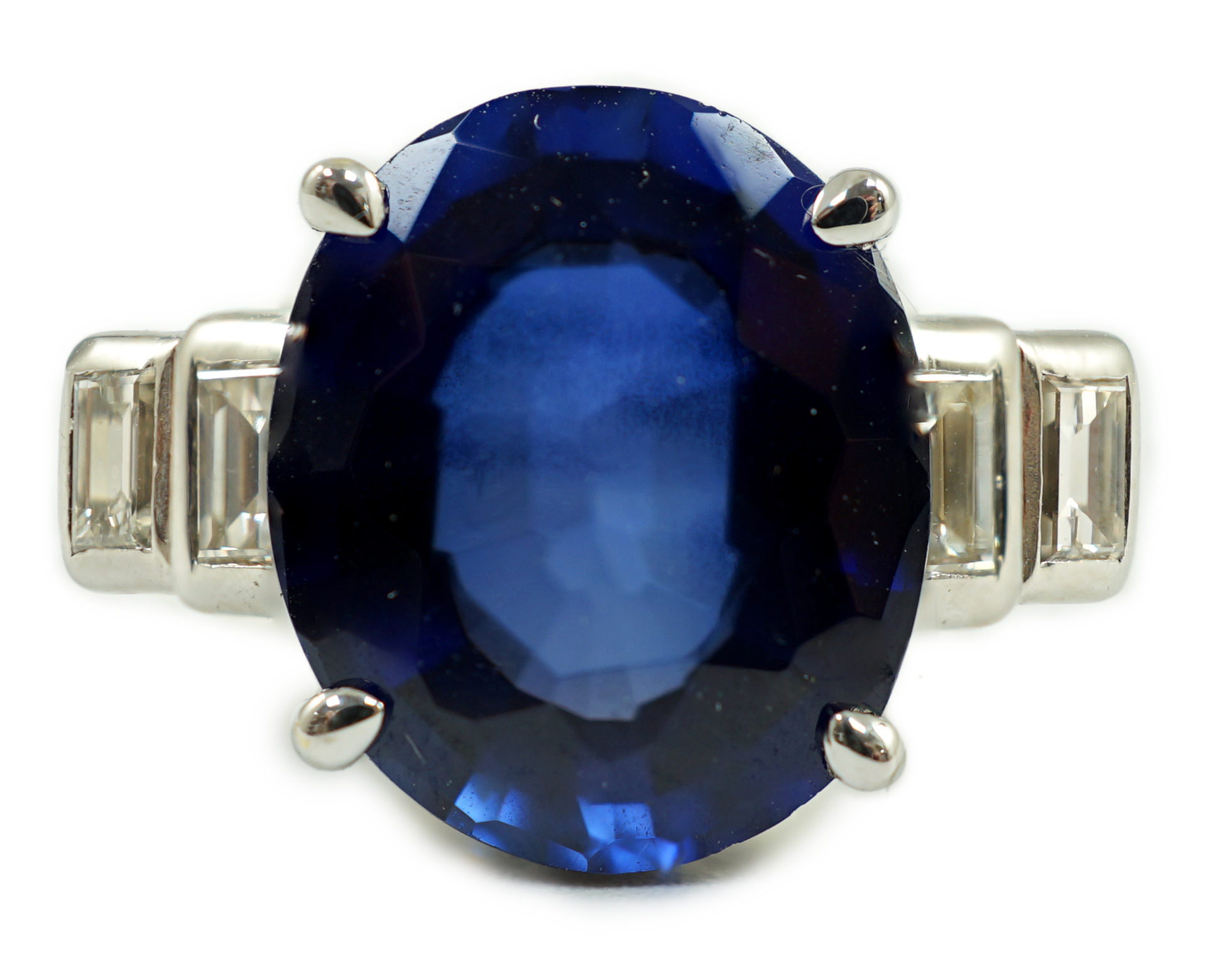 A platinum and single stone oval cut sapphire set cocktail ring, with graduated four stone baguette cut diamond set shoulders